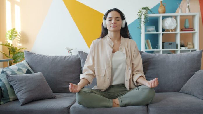 Photo by Vitaly Gariev Woman meditating on couch with headphones on